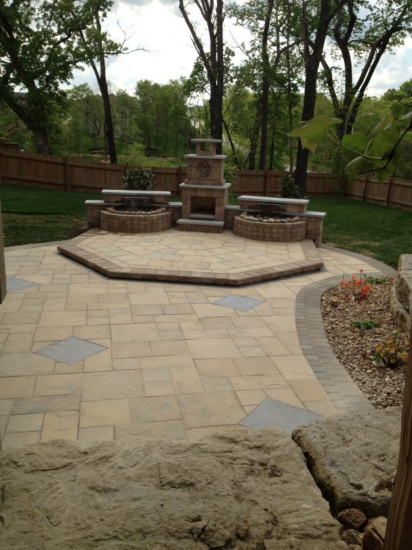 Photo of a landscape design featuring a patio, elevated seating area with a fire feature flanked by a waterfall feature on each side. Designed and installed by Full Features Landscape and Garden Center, Smithville, MO.