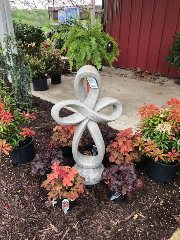 Breast cancer memorial cross statue, surrounded by potted plants of various colors and sizes. On display at Full Features Garden Center.