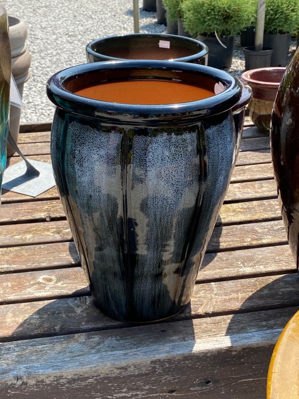 Large brown, gray and neutral tones flower pot with vertical pattern. Displayed on a wooden shelf at Full Features Garden Center. Portions of other flower pots and plants in background.