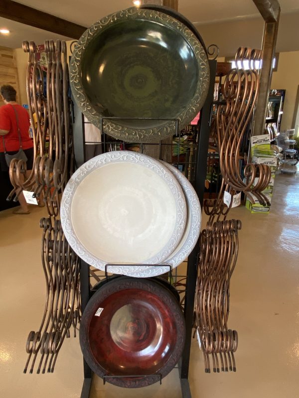 Indoor display of two-piece bird baths. Base is foldable decorative brass-colored iron, with ceramic bowls of white, brick red and olive green colors. On display at Full Features Garden Center.
