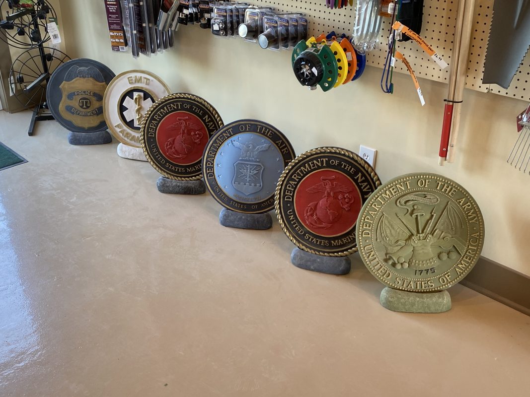 Floor display of plaques recognizing law enforcement, emergency medical services, army, navy, and air force personnel. Background includes portion of wall display of small gardening accessories.